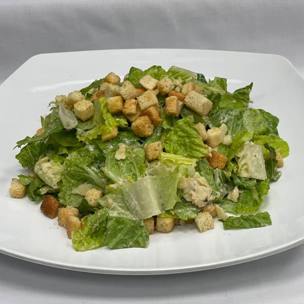 Fresh Caesar salad with crisp romaine lettuce, creamy dressing, and golden croutons on a white plate.