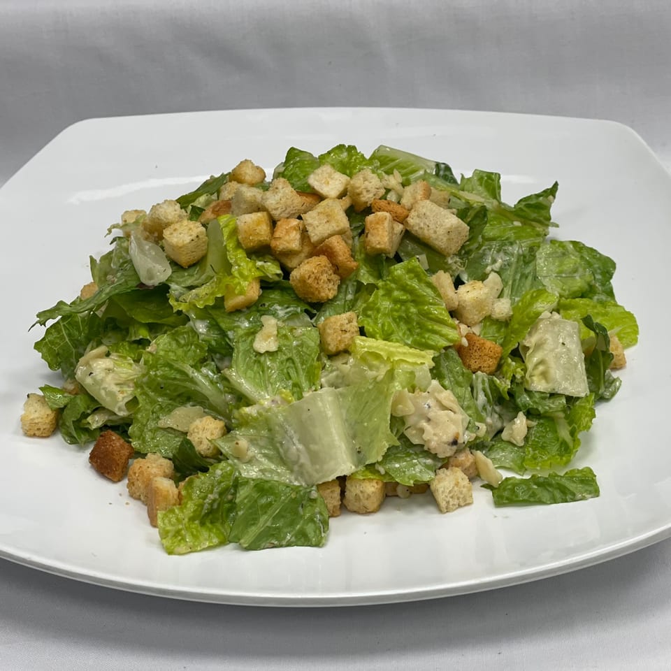 Fresh Caesar salad with crisp romaine lettuce, creamy dressing, and golden croutons on a white plate.