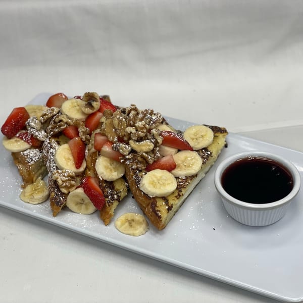 French toast topped with strawberries, bananas, walnuts, powdered sugar, and a side of syrup.