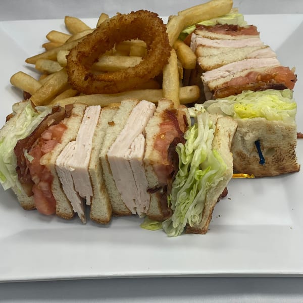 Club sandwich with turkey, bacon, lettuce, and tomato, served with french fries and an onion ring.